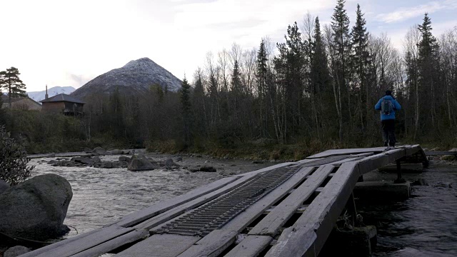 一个男人穿过一个美丽的公园。他在桥上过了那条山河。美丽的山景。视频素材