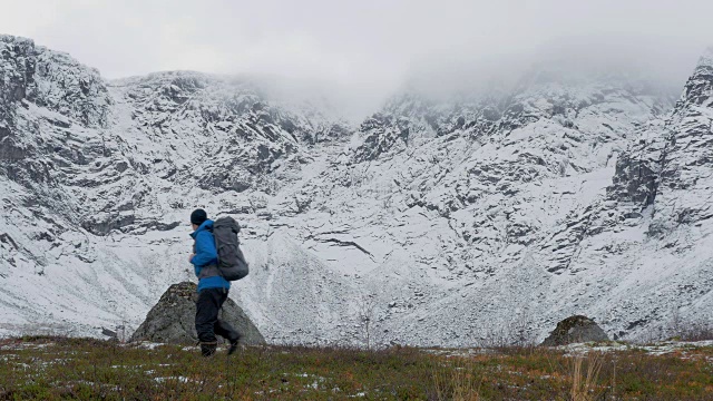 一个人背着双肩包，独自一人，在山里旅行。它沿着白雪覆盖的高峰而行。视频素材