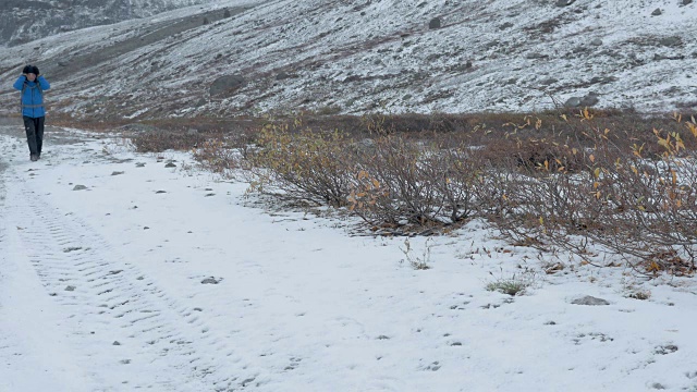 一个人在山里旅行。他走在一条下雪的路上。视频素材