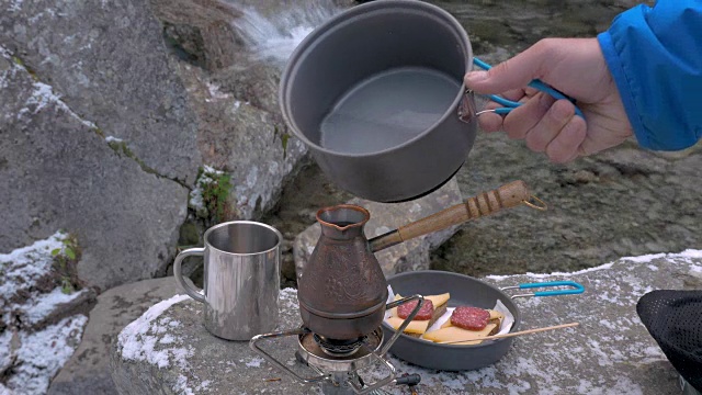 水倒进咖啡壶。特写。在山间的河边吃午餐。视频素材