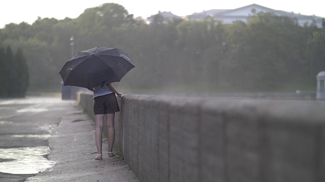 孤独的女孩撑着伞走在雨天的街道上，慢镜头视频素材