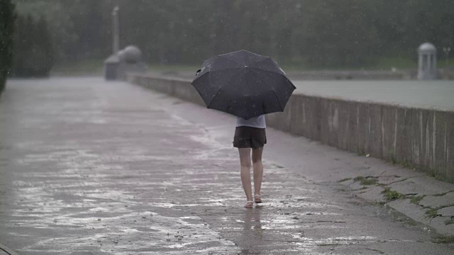 孤独的女孩撑着伞走在雨天的街道上，慢镜头视频素材