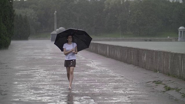 孤独的女孩撑着伞走在雨天的街道上，慢镜头视频素材