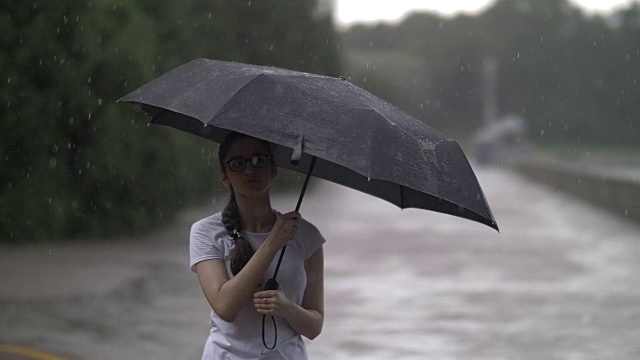 女孩在雨天里捻着伞，看着雨点打在伞上，秋天的心情，慢动作，户外视频素材