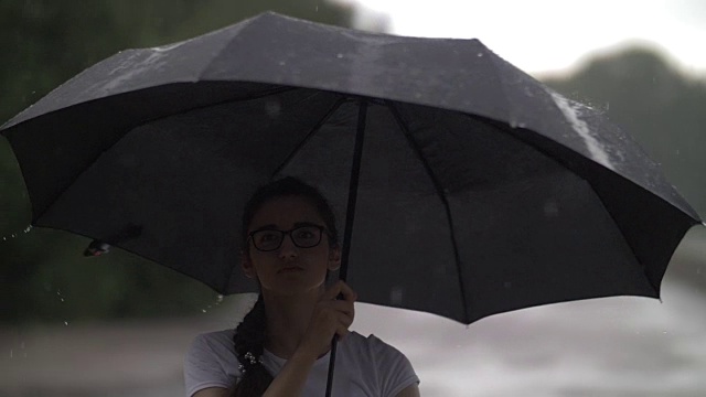 女孩在雨天里捻着伞，看着雨点打在伞上，秋天的心情，慢动作，户外视频素材