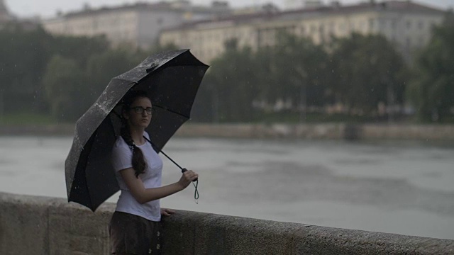 孤独的女孩撑着伞走在雨天的街道上，慢镜头视频素材