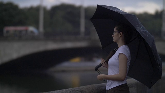 悲伤的女孩撑着伞站在小河旁的小桥后面，想着什么，雨停了，在户外视频素材