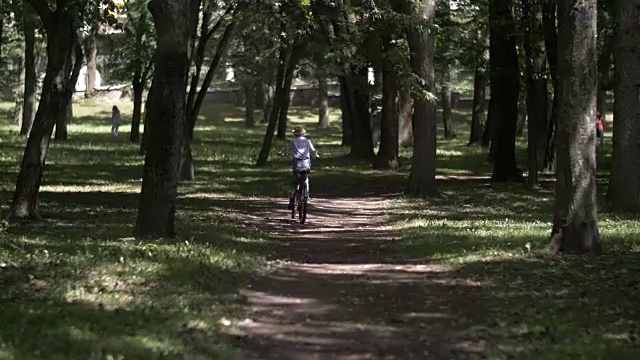 戴着帽子的快乐男孩在城市公园里骑自行车，在户外视频素材