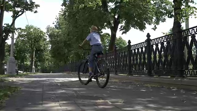 戴着帽子的快乐男孩在城市公园里骑自行车，在户外视频素材