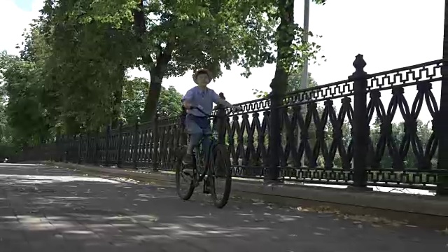 戴着帽子的快乐男孩在城市公园里骑自行车，在户外视频素材