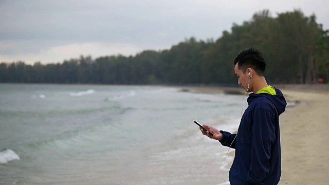 帅哥在海滩上用智能手机跑步，亚洲男人在海滩上跑步。视频素材