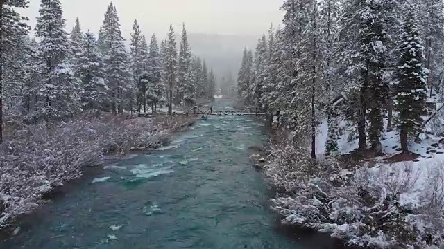 航拍:雪天飞向翡翠河上的木桥。视频素材