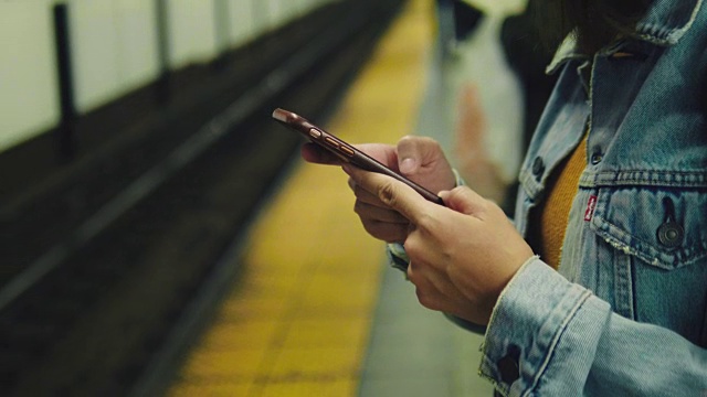 年轻的亚洲女子在地铁站台上用手机等待和发短信。视频素材