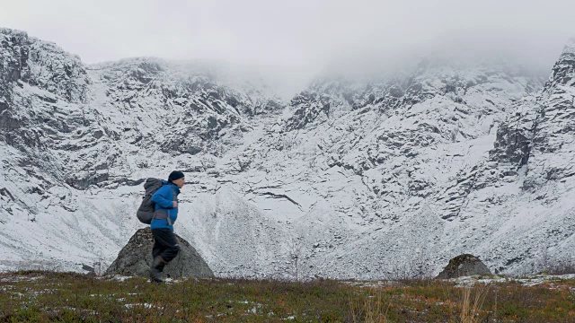 一个人背着双肩包，独自一人，在山里旅行。它沿着白雪覆盖的高峰前进。视频素材