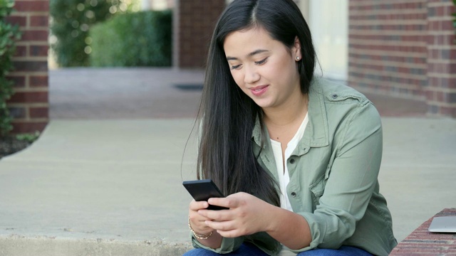 自信的女大学生在校园里使用智能手机视频素材