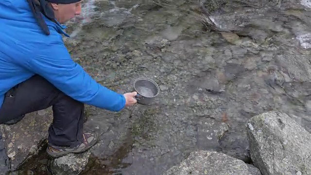 一名男子在徒步旅行中从山间的河流中取水做饭。视频素材