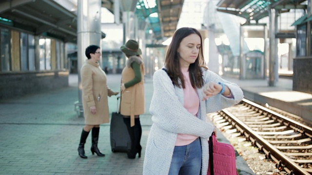 一个女孩在火车站的月台上等候火车。人们在后台说再见视频素材