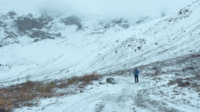 一位游客在一条被雪覆盖的小路上散步。一个人在高山徒步旅行时走在雪地里。视频素材