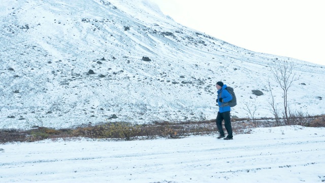 一个男人背着双肩包在下雪的路上旅行。它沿着一个高高的山脊。视频素材