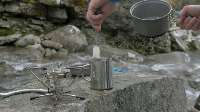 旅行者从煤气灶上拿出壶，把开水倒进杯子里。他使茶。特写镜头视频素材