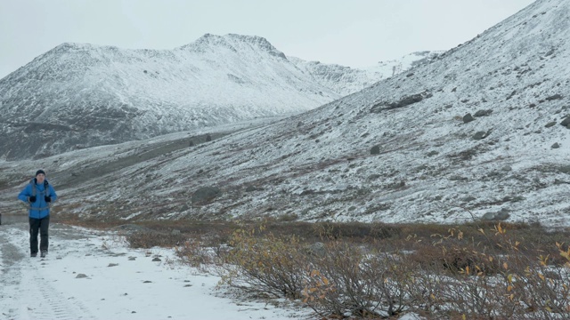 一个背着双肩包的男人正走在山中的一条积雪的路上。视频素材