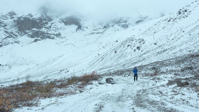 一个普通的中年人在山路上旅行。他一个人走在下雪的路上。视频素材