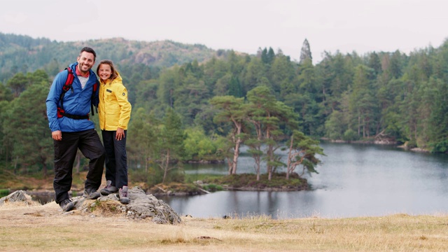 英国湖区，白人父亲和女儿站在乡间湖边的岩石上望着镜头视频素材