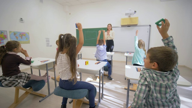 儿童上学时，年轻教师女教师在教室的课桌旁黑板上为幼儿进行认知课视频素材