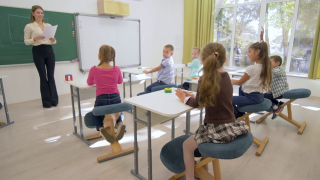 孩子们学习时，年轻的教师女士在学校的课桌上为好学生进行认知课视频素材