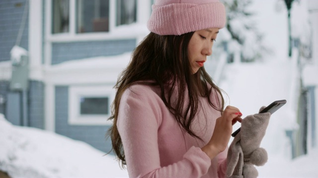 亚洲千禧一代在白雪覆盖的街道上使用智能手机的特写视频素材