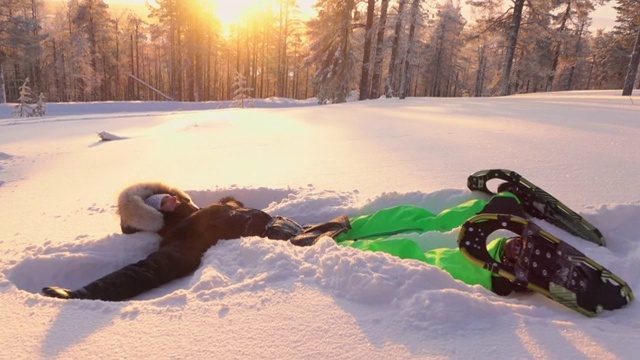 特写:在金色的夕阳下，快乐的女孩在新鲜的雪中制作雪天使视频素材