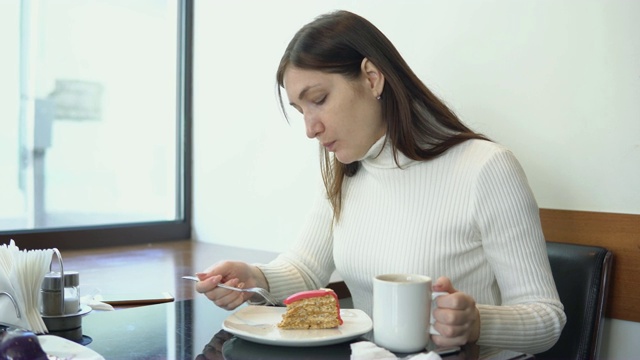 年轻女子在咖啡馆喝咖啡吃蛋糕。视频素材