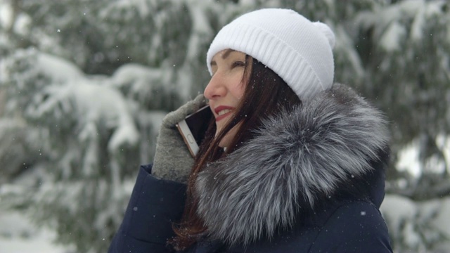 一个年轻的女人正在冬天的森林里打电话。在新鲜空气中散步视频素材