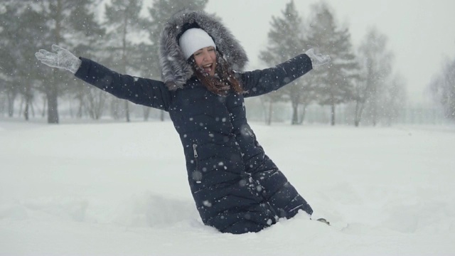 一个年轻女子摔倒在雪堆里。在冬季公园里愉快地散步视频素材