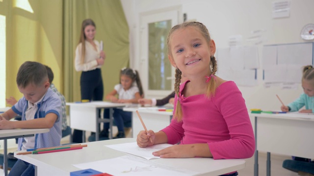 肖像上的女学生绘图课在轻教室坐在桌子后面的背景同学和年轻的老师视频素材