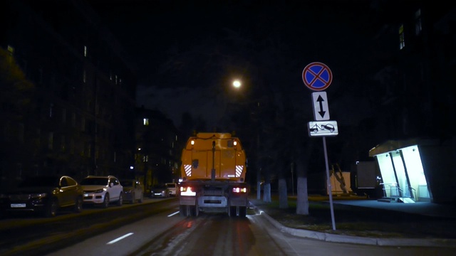 汽车吸尘器在夜间在镜头前清扫街道，然后开车离开。视频素材