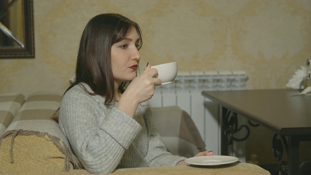 一个年轻女子在咖啡馆里用一个白色的杯子喝咖啡。视频素材