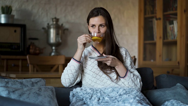 漂亮的女人坐在沙发上，裹着毯子喝着茶视频素材