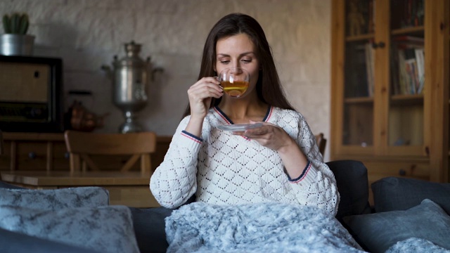 漂亮的女人坐在沙发上，裹着毯子喝着茶视频素材