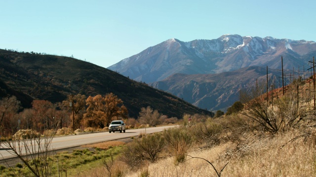 拍摄的雪顶犹他山在远处的框架山谷与电力线路和车辆在公路上行驶在一个晴朗的蓝天下视频素材