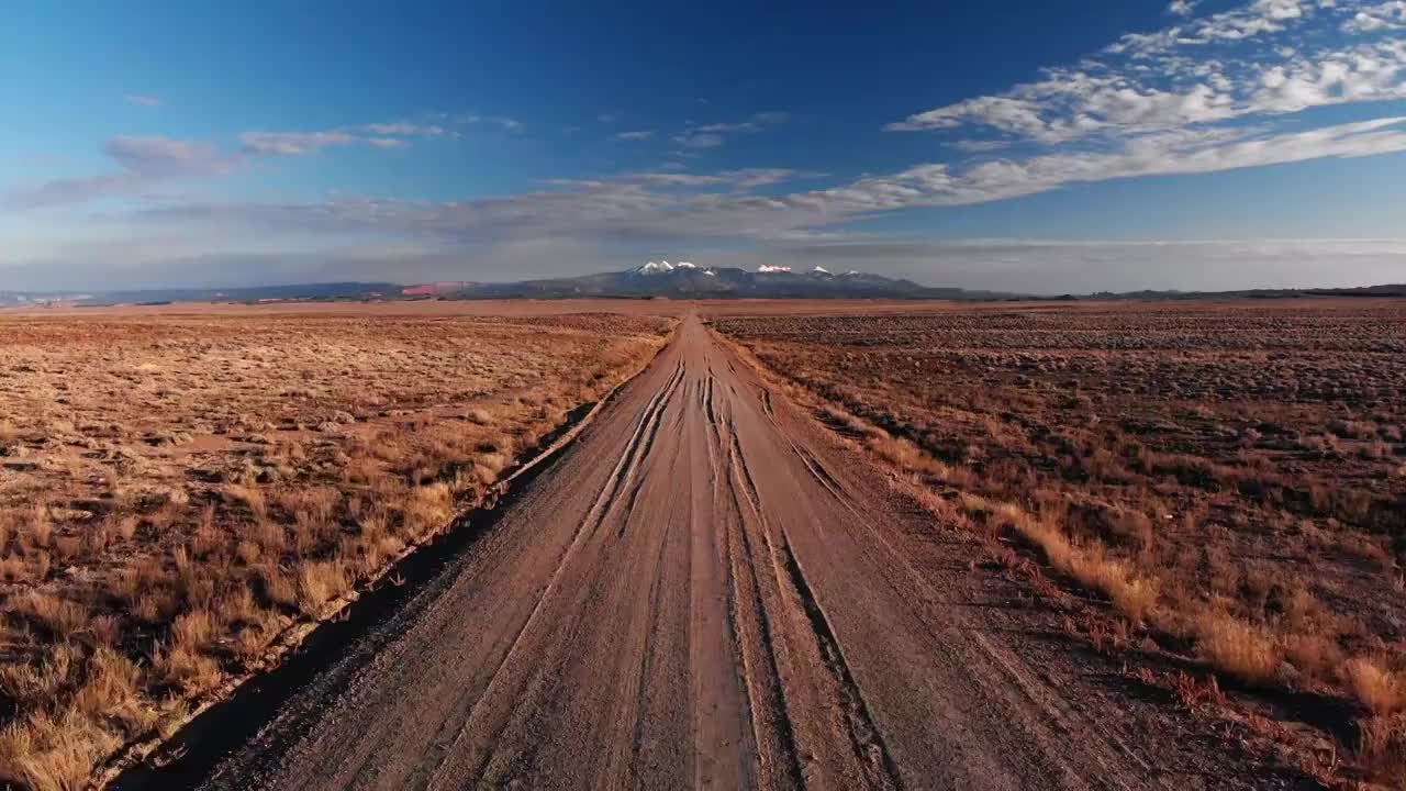 前进无人机拍摄的消失点土路与山脉的背景摩押外，犹他州与沙漠平原在蓝天下的日落/日出视频素材