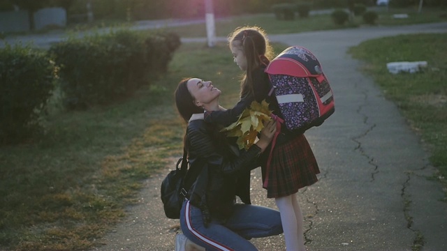 一个女人在学校见她的小女儿。一个穿着校服背着背包的女孩拥抱和亲吻她的妈妈。慢动作视频素材