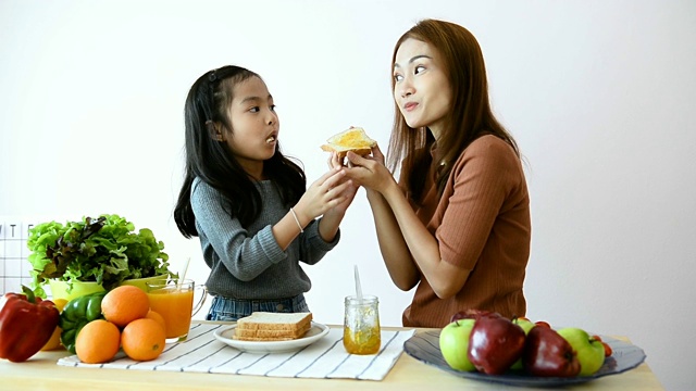 妈妈给女儿在面包上涂果酱。视频素材