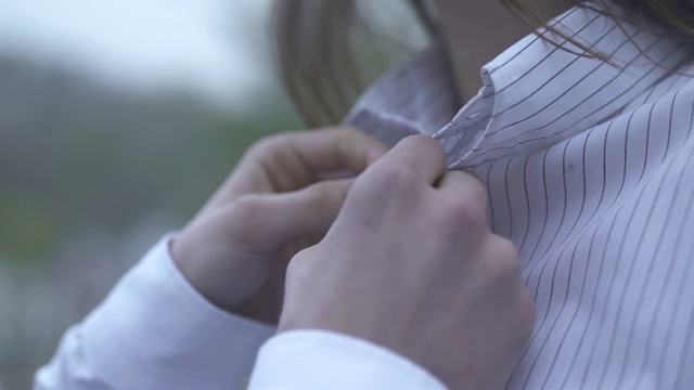 男人的手系住一个女孩的衬衫上的纽扣，关心男人和女朋友一起花时间在一起相爱的夫妇视频素材