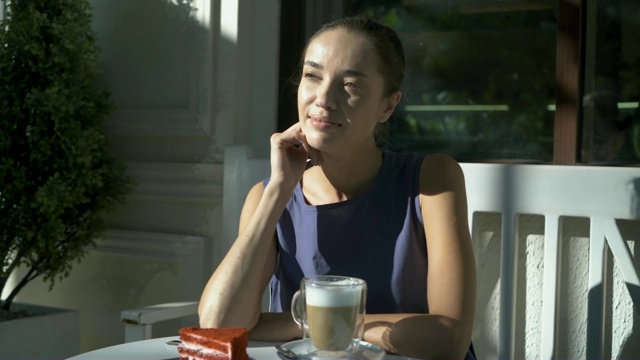 美丽快乐的年轻女子喝咖啡或茶在咖啡馆在夏天的早晨，看着相机。视频素材