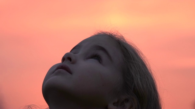 孩子在大自然中仰望天空。小女孩祈祷着仰望着紫色的天空，带着希望，特写。视频素材