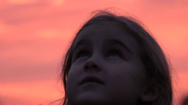 孩子在大自然中仰望天空。小女孩祈祷着仰望着紫色的天空，带着希望，特写。视频素材