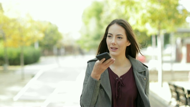 一个女人在公园里用电话语音识别走路视频素材