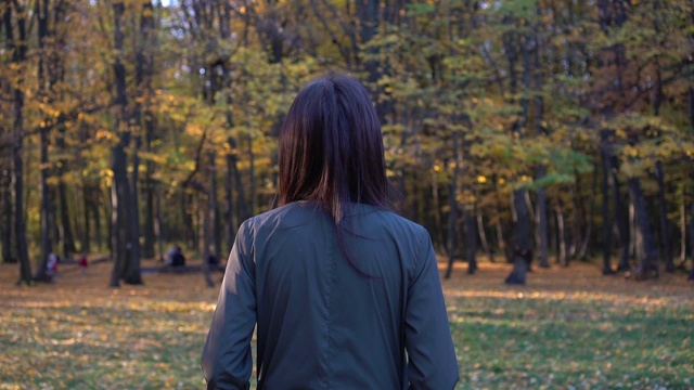 从背影看年轻的白人妇女走到街上在一个多彩的秋天公园，享受秋天的树叶。视频素材