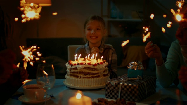 可爱的小女孩在餐桌上庆祝生日。她睁开眼睛，看到了生日蛋糕，非常高兴。快乐的孩子，朋友和家人在晚上视频素材